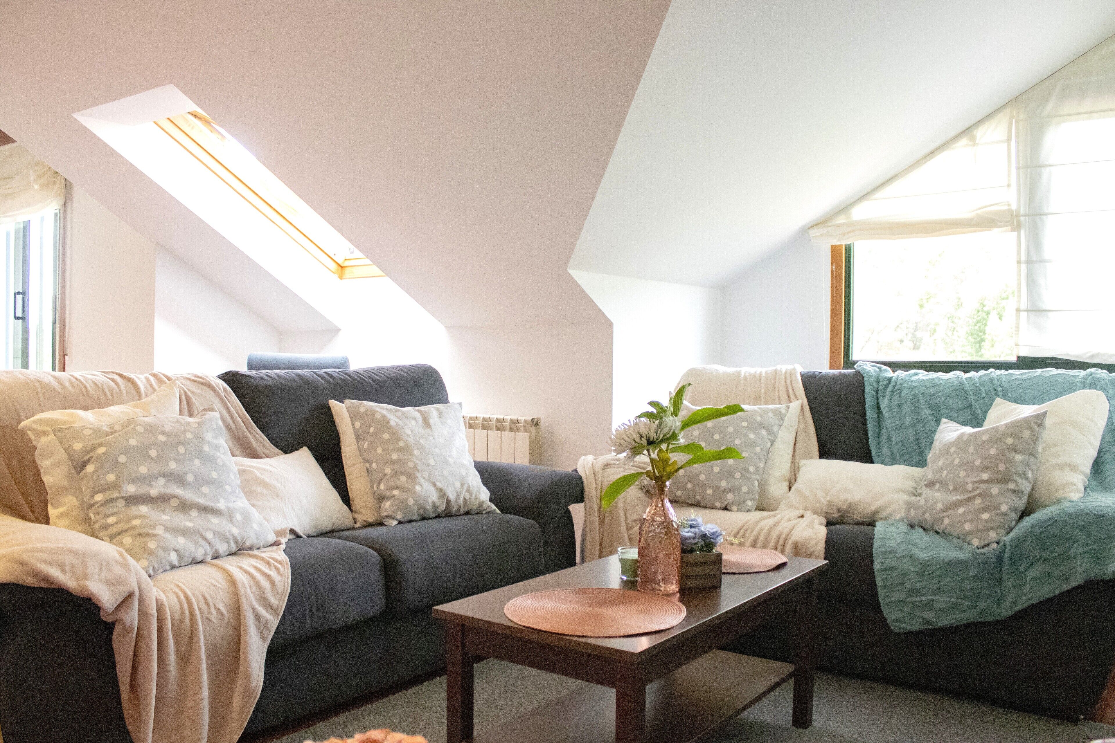 A modern living room with a dark grey sofa, a coffee table, and a large window providing natural light.