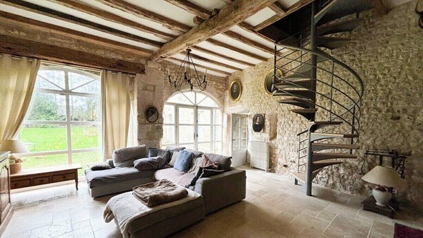 A rustic room with exposed wooden beams, a stone wall, a spiral staircase, and a large window with a view of greenery. - Beautiful stone barn with year-round heated pool<br>Magnificent setting in the heart of the Perche region (Belforêt-en-Perche)