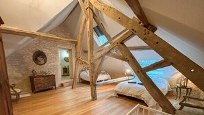 A loft bedroom with exposed wooden beams, a wooden floor, a bed, a dresser, and a small table. - Beautiful stone barn with year-round heated pool<br>Magnificent setting in the heart of the Perche region (Belforêt-en-Perche)