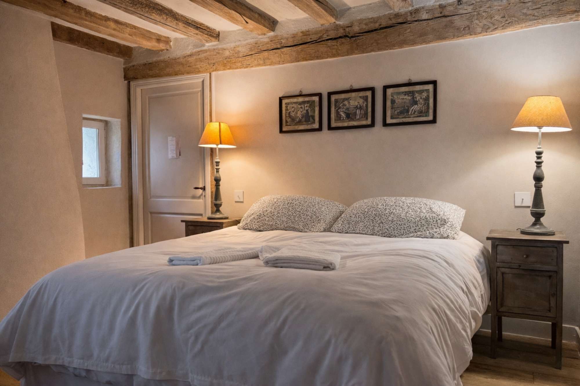 A bedroom with a bed, two bedside lamps, a nightstand, and three framed pictures on the wall.