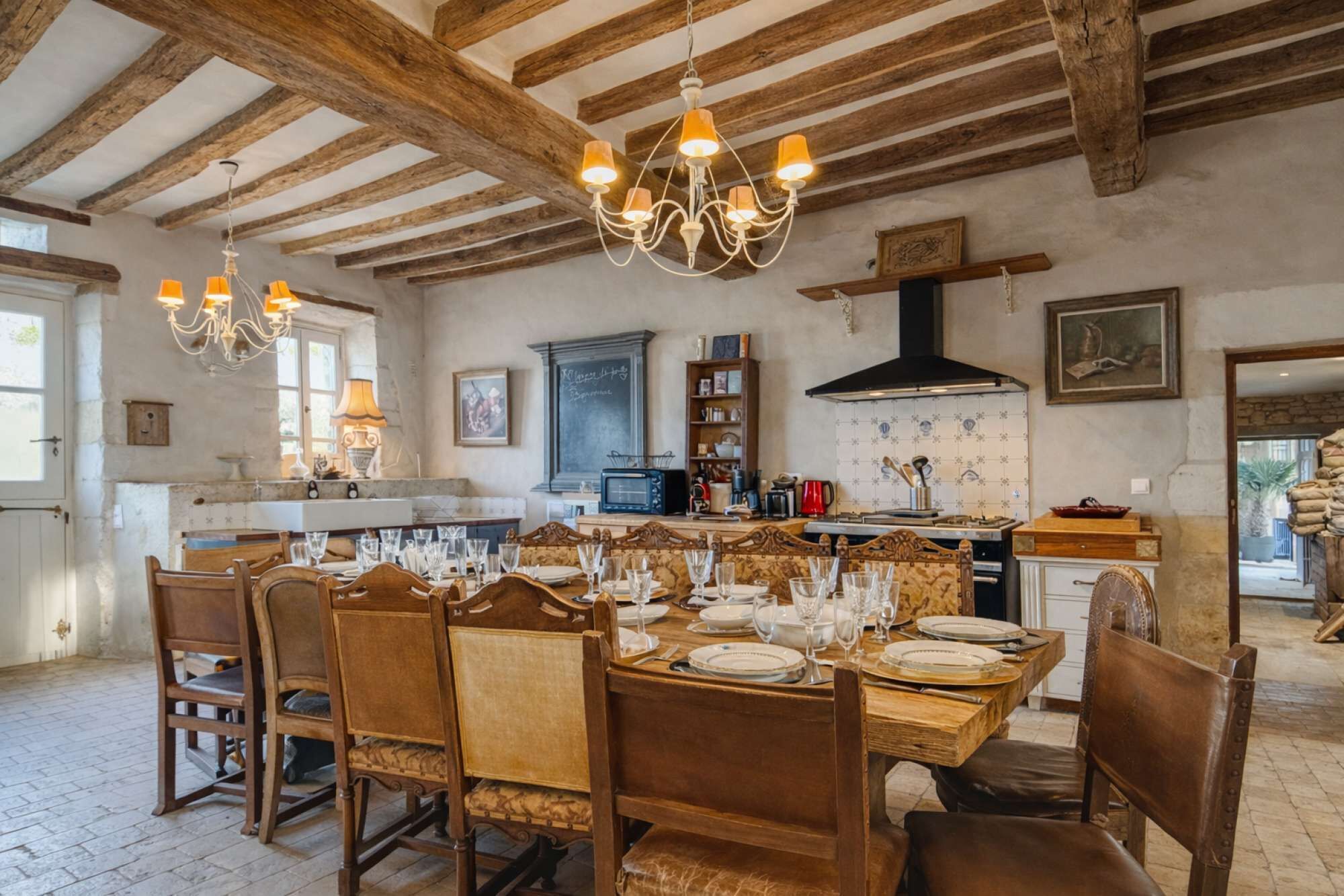 Un comedor rústico con muebles de madera, una araña y una cocina al fondo.