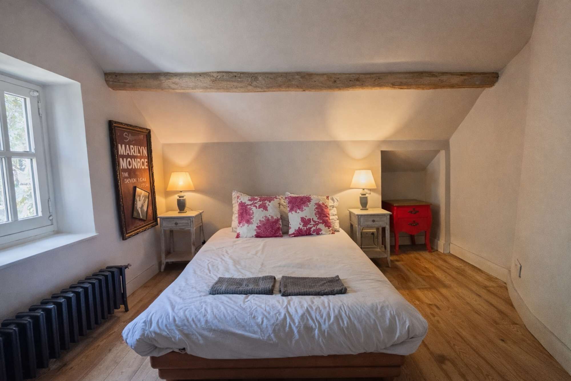 Un dormitorio con una cama grande, dos mesitas de noche con lámparas, un aparador rojo y un radiador.