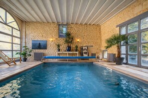 Piscina interna con pareti in pietra, una panca e piante in vaso.