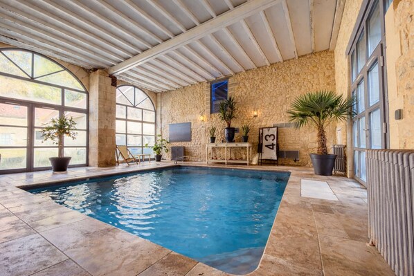 Una piscina interna con pareti in pietra, pavimento piastrellato e piante in vaso.