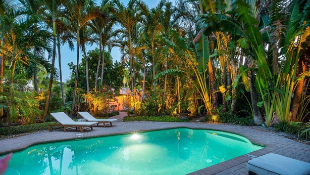 A swimming pool with lounge chairs and a small table, surrounded by lush tropical vegetation.