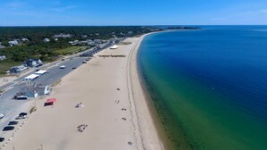 Une vue aérienne d’une plage avec un parking, des bâtiments et un océan bleu azur.