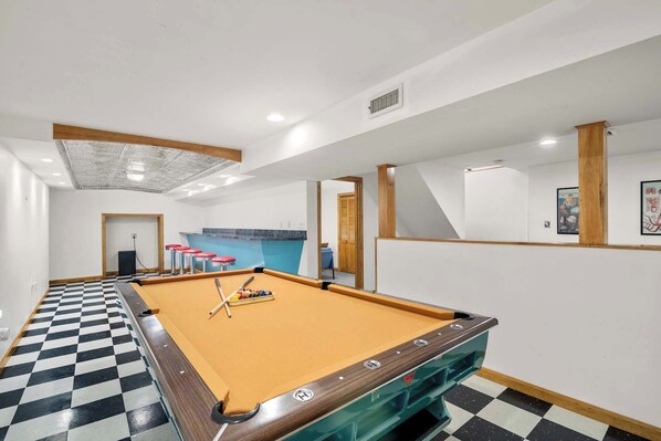A pool table with a checkered floor, a blue wall, and a door leading to another room.