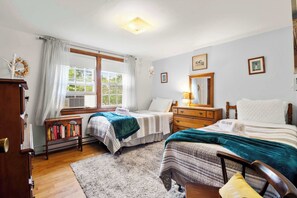 Een slaapkamer met twee bedden, een houten dressoir, een boekenkast, een raam met gordijnen en een plafondlamp.