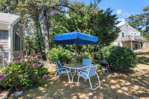 Een terras met een tafel, stoelen, een blauwe parasol en een barbecue.