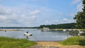 A calm lake with boats, a sandy shore, and a house in the background. - Cozy Cottage Walk to Nauset Beach! (Orleans)