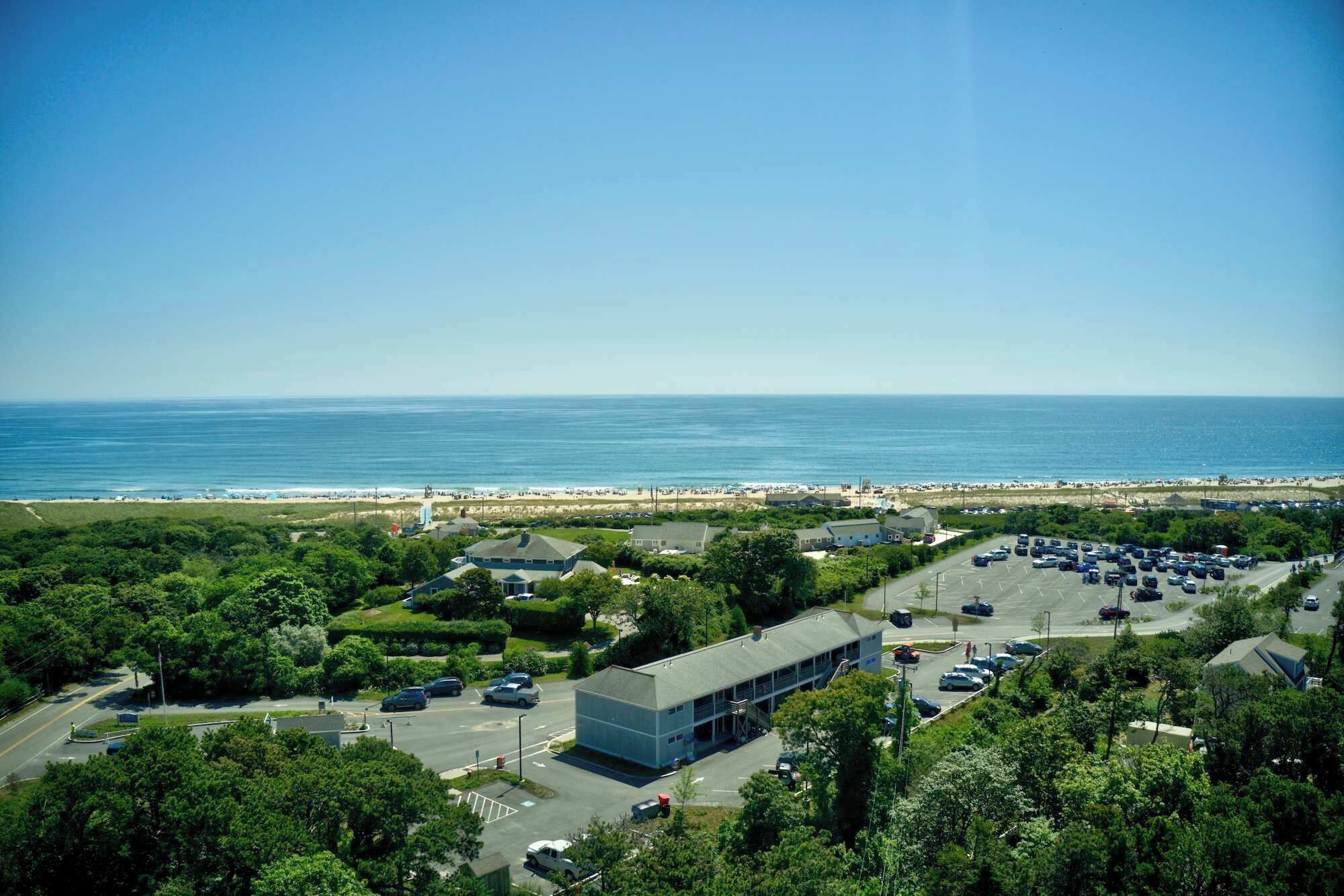 Vista costera con aparcamiento, un edificio de techo plano y una playa al fondo.