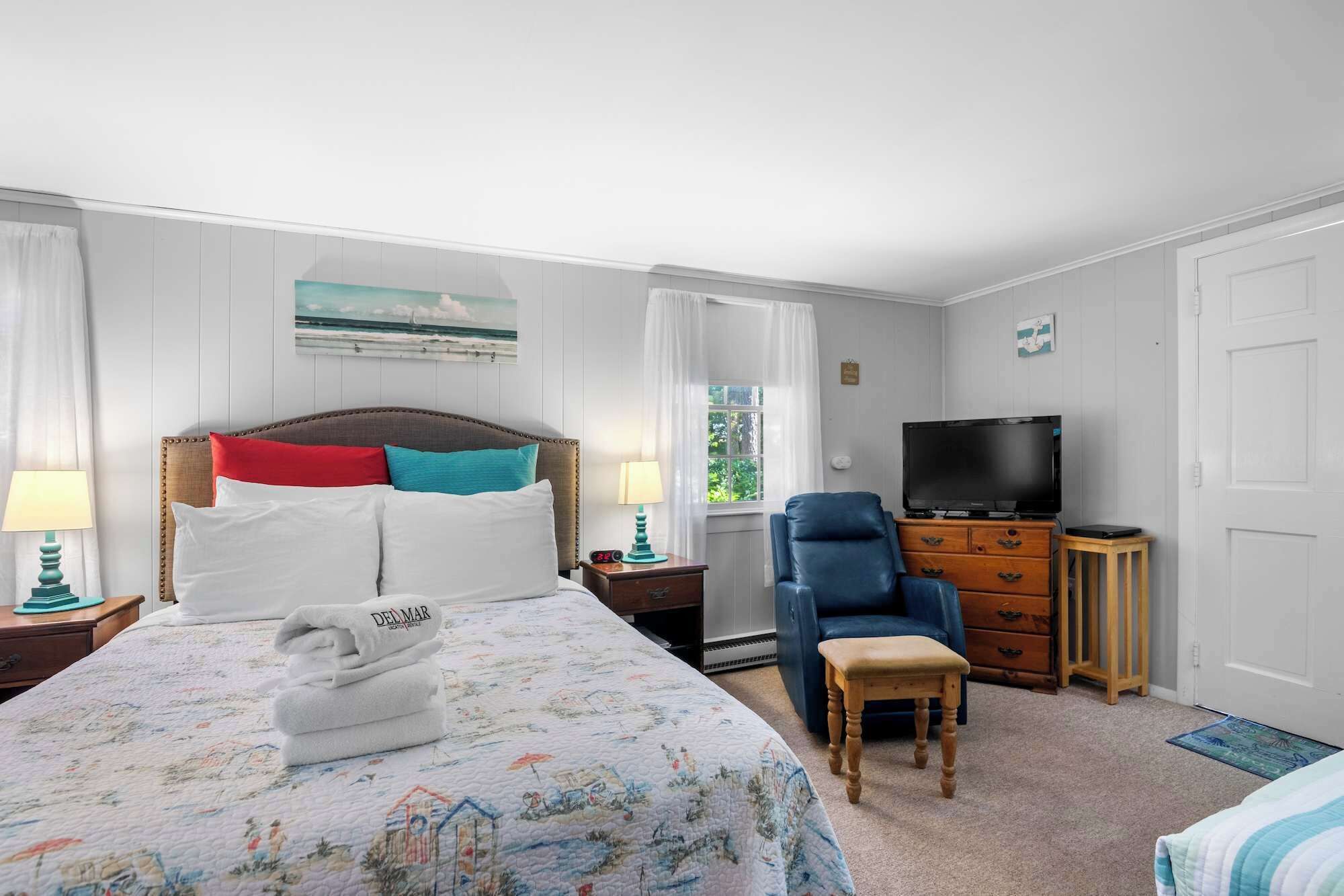A hotel room with a bed, a TV, a chair, a small table, and a window with curtains.