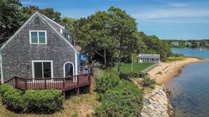 A coastal house with a wooden deck, a stone wall, and a view of the beach and water.