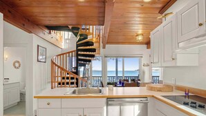 A modern kitchen with a wooden ceiling, white cabinetry, and a view of the sea.