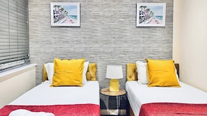 Habitación de hotel con dos camas, cada una con almohadas amarillas, una manta roja y una toalla blanca. Dos cuadros en la pared muestran una escena de playa.