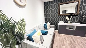 Una sala de estar moderna con un sofá, almohadones decorativos, una mesita de centro, un reloj, un espejo y un papel tapiz estampado.