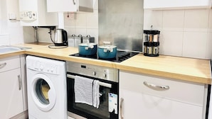 Una cocina moderna con armarios blancos, una campana de acero inoxidable, horno empotrado, lavadora y cafetera.