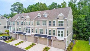 A multi-story residential building with a symmetrical facade, multiple garage doors, and a well-maintained lawn. - Family Fun house at Barefoot Resort & Golf (North Myrtle Beach)