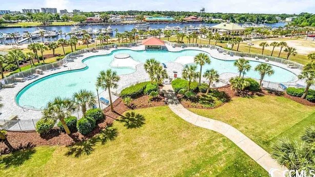 A large, curved swimming pool surrounded by palm trees and a small building, with a marina and cityscape in the background. - Family Fun house at Barefoot Resort & Golf (North Myrtle Beach)