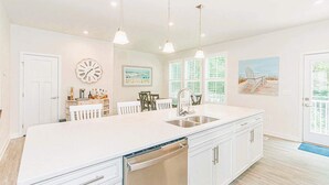 A spacious kitchen with a large island, white cabinetry, pendant lighting, and a view of the outdoors through large windows. - Family Fun house at Barefoot Resort & Golf (North Myrtle Beach)