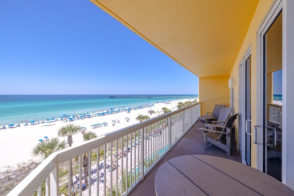 A balcony with a view of a beach and ocean, featuring a pool and lounge chairs. - 401E Beach Service Included! End Unit! (Panama City Beach)