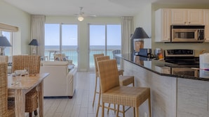 A kitchen with a microwave, stove, and dining area with wicker chairs and a table. - 401E Beach Service Included! End Unit! (Panama City Beach)