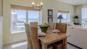 A dining area with wicker chairs, a wooden table, and a view of the beach. - 401E Beach Service Included! End Unit! (Panama City Beach)