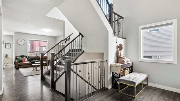 A modern living room with a staircase, a bench, and a window with blinds.