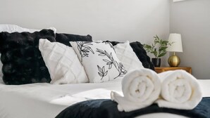 A neatly made bed with rolled towels, black and white pillows, and a bedside plant.