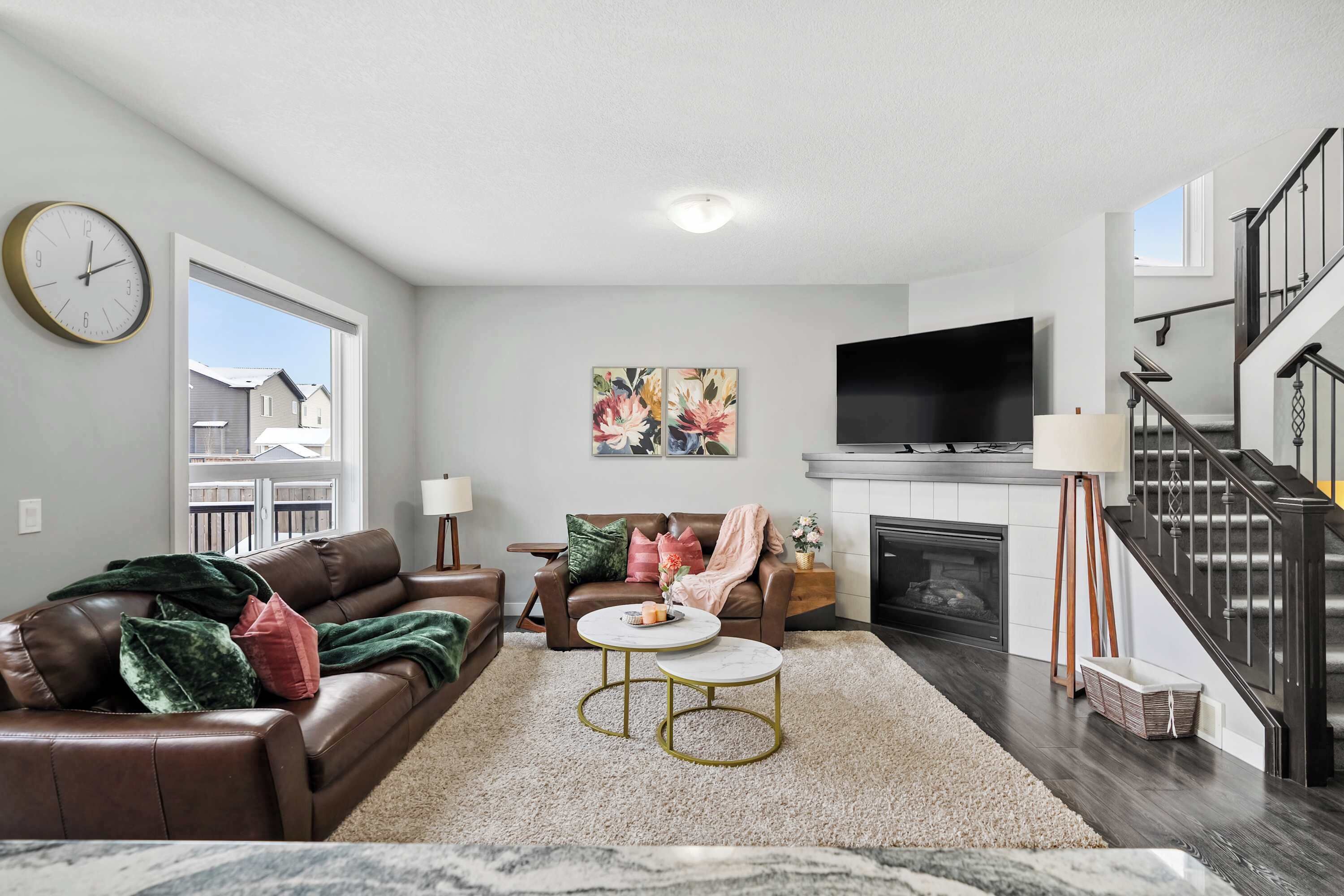 A living room with a brown leather sofa, two round coffee tables, a fireplace, and a TV mounted on the wall.