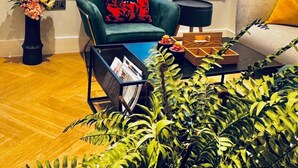 A living room with a green armchair, a sofa with yellow cushions, a black side table, a floor lamp, a large window with blinds, and a potted plant. - London Charm - Central London Apart Soho Mayfair (London)