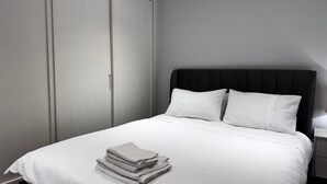 A neatly made bed with white linens and pillows, a stack of folded towels, and a dark headboard. - London Charm - Central London Apart Soho Mayfair (London)