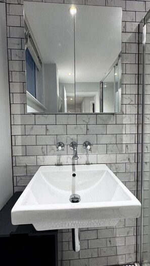 A bathroom with a white sink, a mirror above it, and a tiled wall. - London Charm - Central London Apart Soho Mayfair (London)
