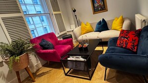 A living room with a red armchair, a blue sofa, and a white sofa with colorful cushions. There is a black coffee table in the center. - London Charm - Central London Apart Soho Mayfair (London)