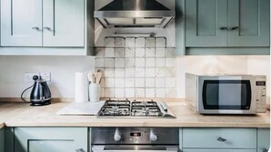 A kitchen with teal cabinets, a gas stove, a stainless steel range hood, a microwave, and a tiled backsplash. - London Charm - Central London Apart Soho Mayfair (London)