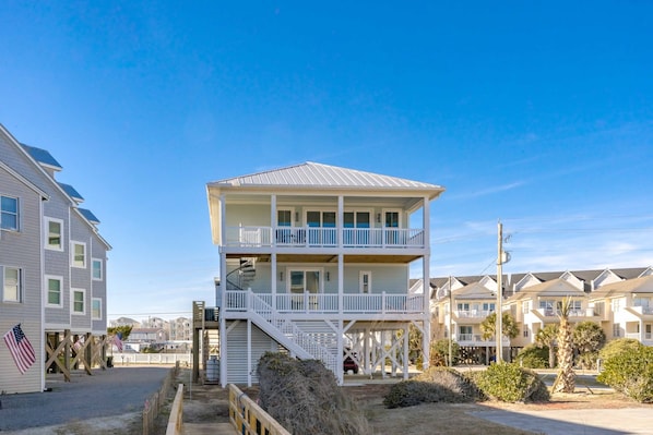 A two-story beachfront building with a balcony, a staircase, and a view of the ocean.