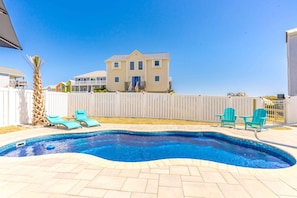 A swimming pool with a tiled deck, two lounge chairs, and a white fence.