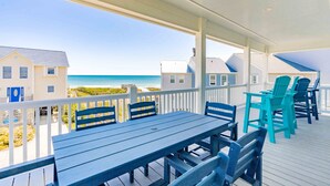A covered outdoor area with a table and chairs, overlooking a beach and buildings. - Dune Just Fine - Gorgeous 5BR Home - Pool, Elevator, Porches & More! (Surf City)