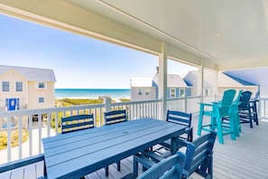 A covered outdoor area with a table and chairs, overlooking a beach and buildings.