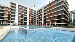 Un hôtel moderne doté d’une grande piscine, de plusieurs étages et d’une terrasse en carrelage autour de la piscine.