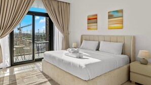 Une chambre d’hôtel moderne avec un grand lit, une vue sur la ville depuis un balcon et deux tableaux abstraits accrochés au mur.