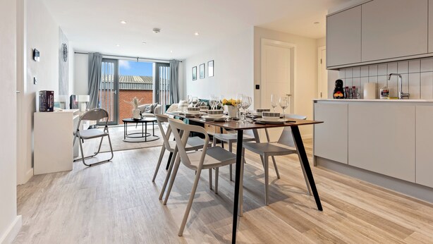 Una cucina moderna con mobili bianchi e un'area pranzo con tavolo e sedie in legno.