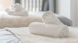 Un letto rifatto con una coperta bianca a trama e asciugamani bianchi arrotolati.