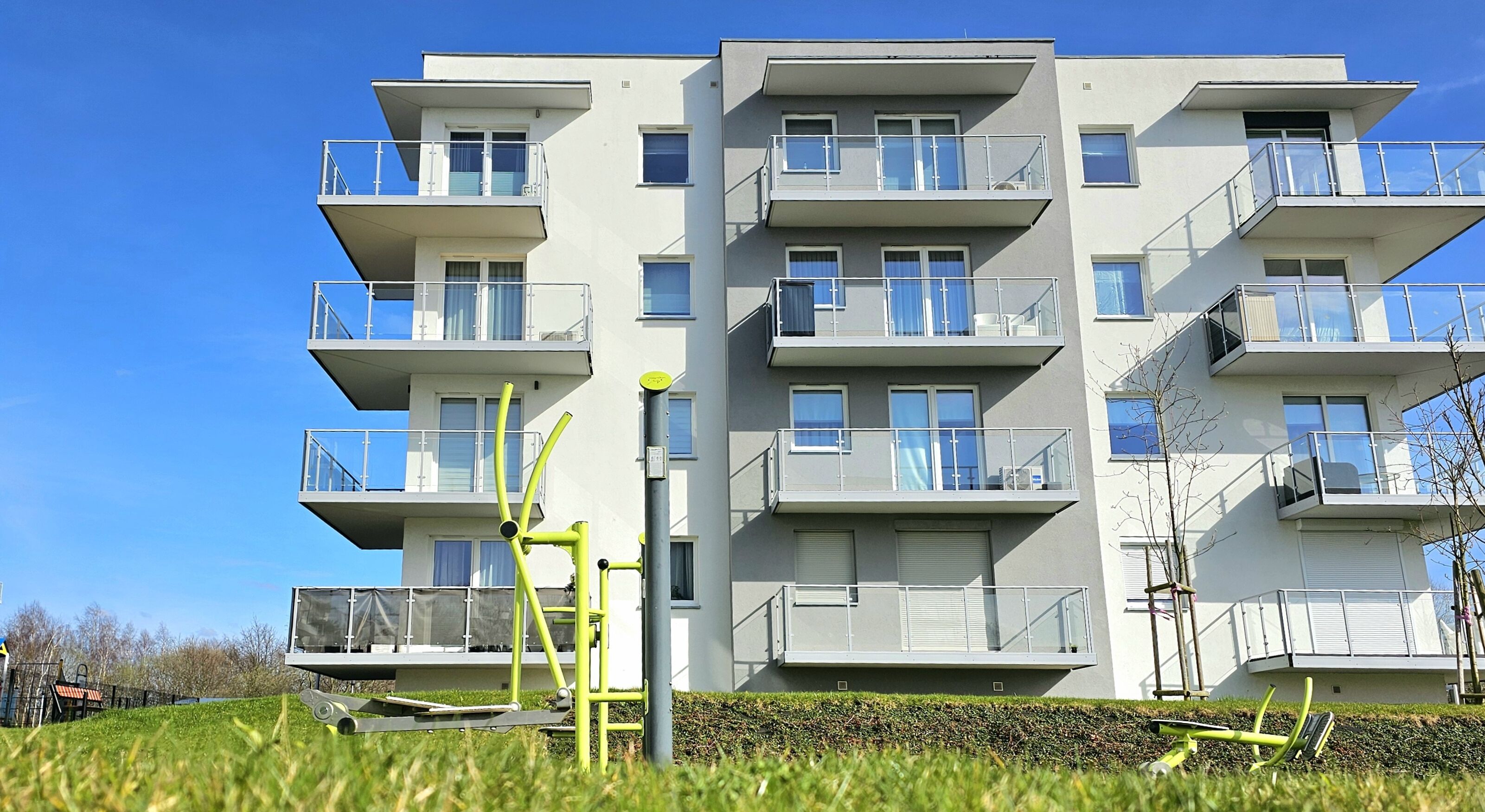 A multi-story residential building with balconies, a flat roof, and a clear blue sky.