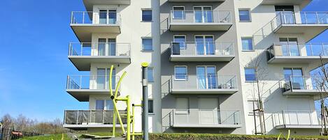 A multi-story residential building with balconies, a flat roof, and a clear blue sky.