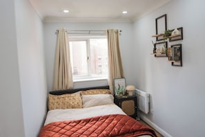 A bedroom with a bed, curtains, a radiator, and wall-mounted shelves with decorative items. - Sienna Haven Sleeps 4 With Parking (Birmingham)