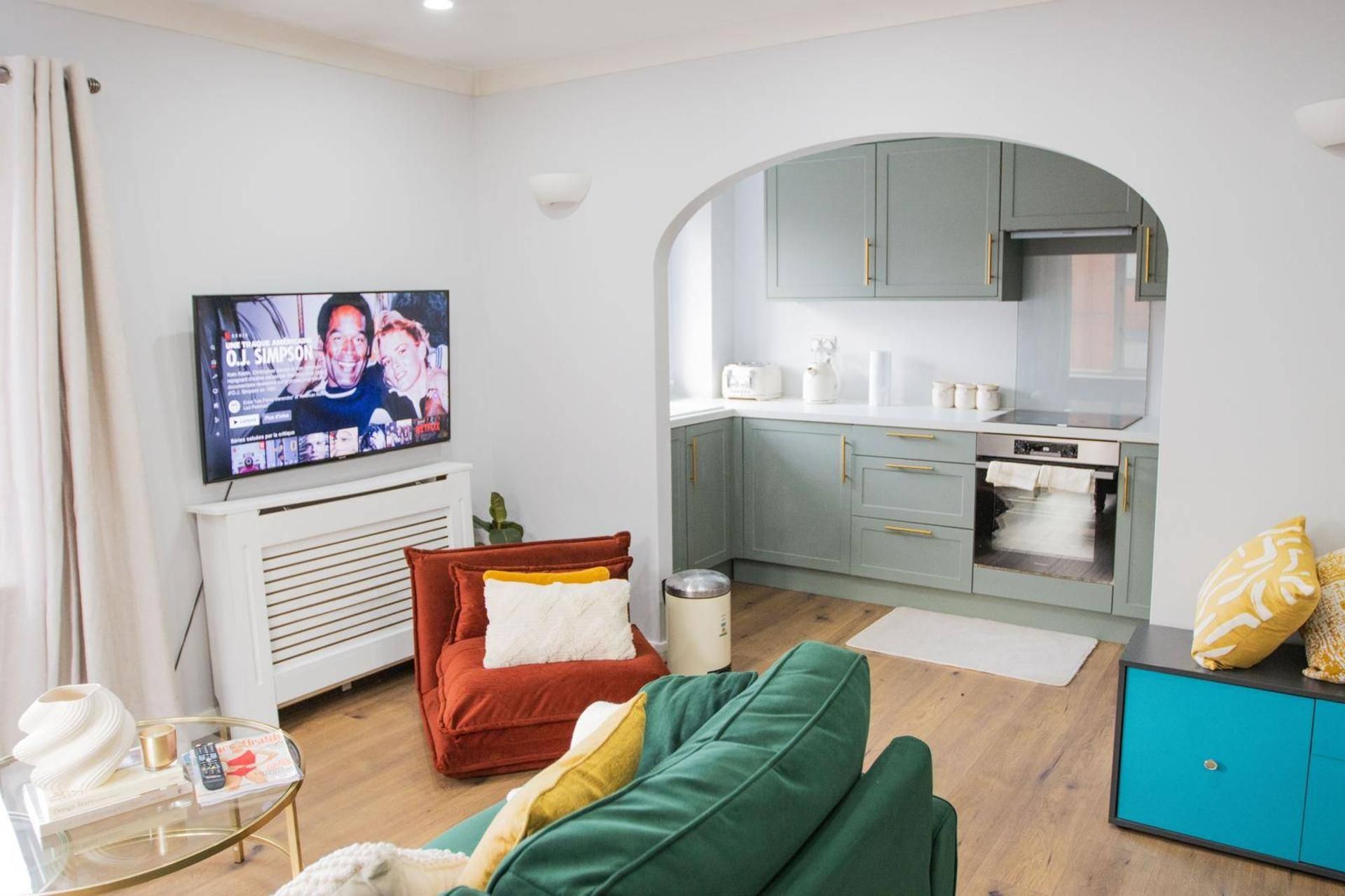 Ein Wohnzimmer mit Fernseher, einer Couch, einem Couchtisch und einer Küchenzeile inklusive Schränke und Geräte.