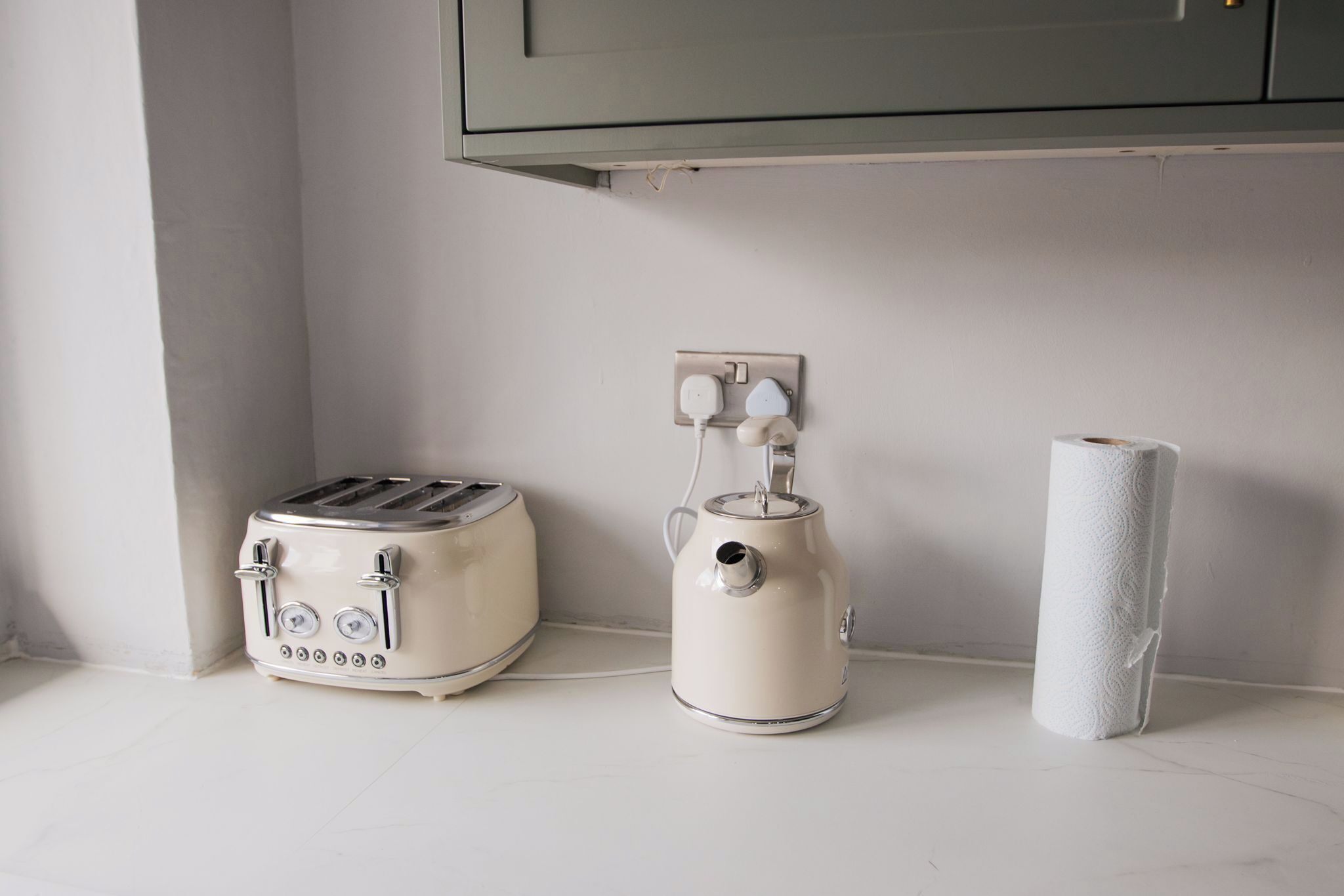 A kitchen with a white toaster, a white kettle, and a roll of paper towels on the counter.