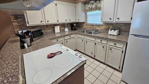 A kitchen with white cabinets, a granite countertop, a built-in microwave, a stove, a sink, and a refrigerator.