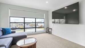 Un salon moderne avec un canapé gris, une table basse ronde et une grande fenêtre donnant sur un parking.